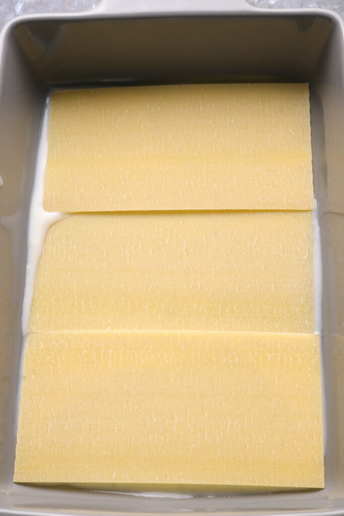 lasagne sheets sitting on top of béchamel sauce in a lasagne tray