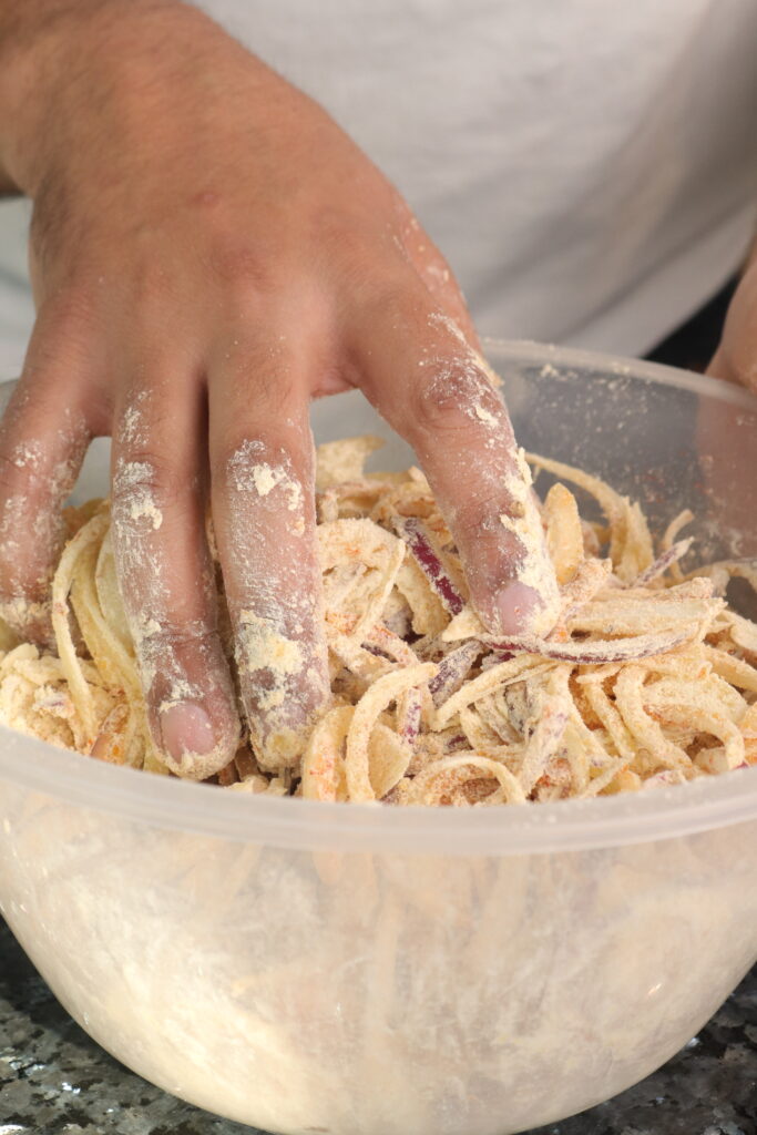 onions being mixed with spices and chickpea flour in a mixing bowl