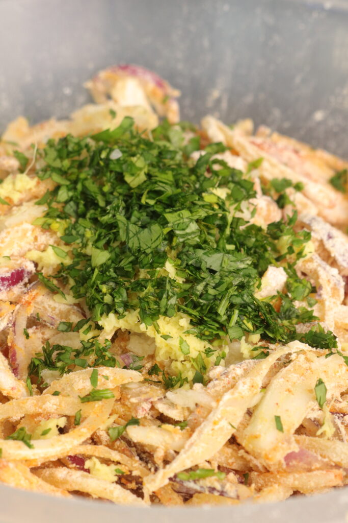 grated garlic, grated ginger, and coriander on top of onions in a mixing bowl