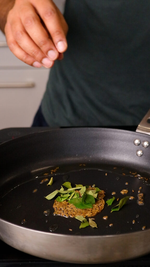 cumin seeds and curry leaves in a pan