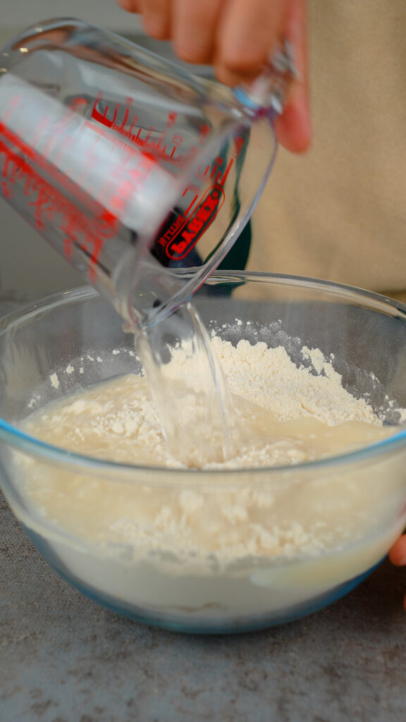 pouring water onto focaccia dry ingredients in a mixing bowl