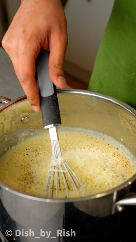 whisking seasonings and cheese into the béchamel sauce