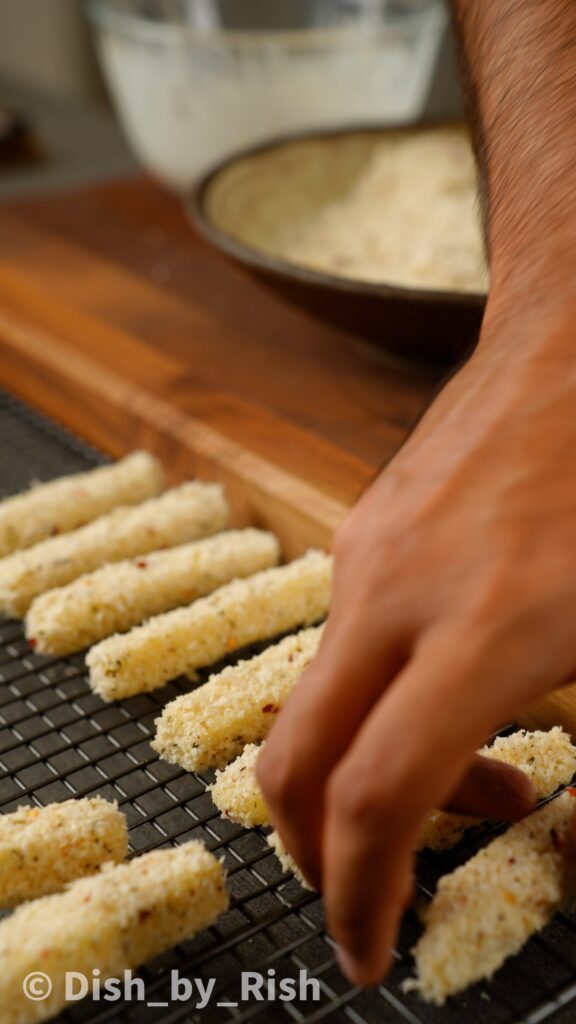 placing mozzarella stick coated in panko breadcrumbs on a wire rack