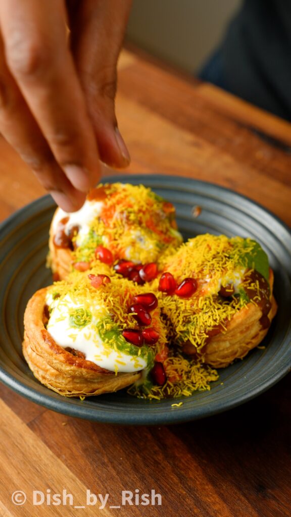 topping vol-au-vent chaat with yoghurt, chutneys, and sev, and pomegranates