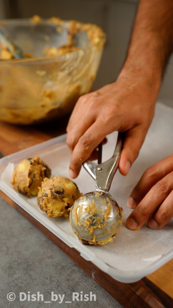 using an ice cream scoop to scoop cookie dough onto lined tray