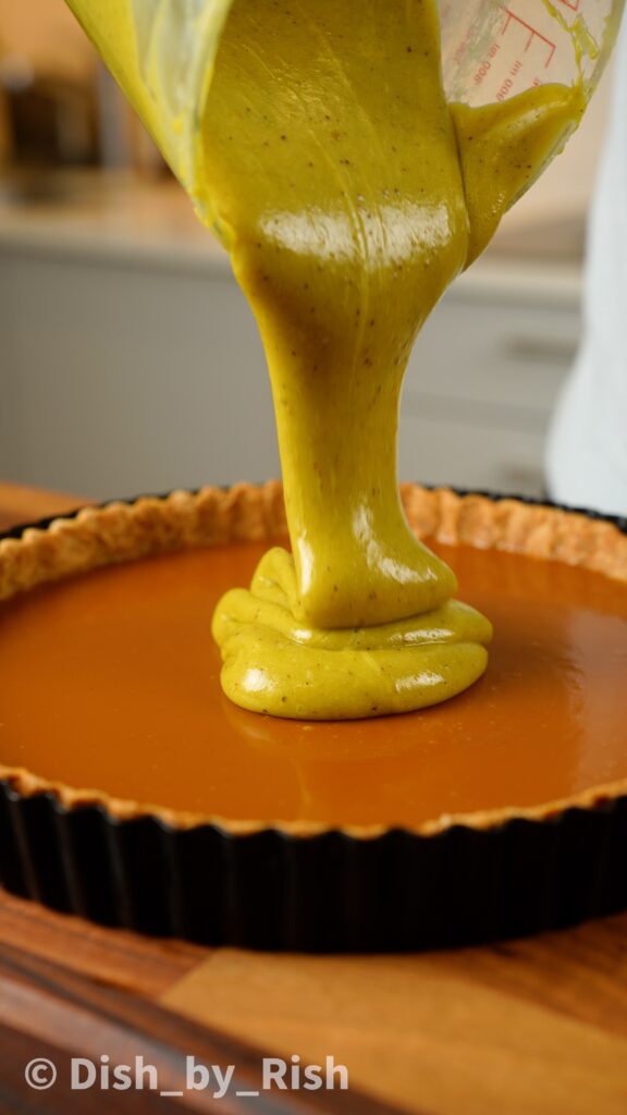 pistachio ganache being poured on top of caramel tart