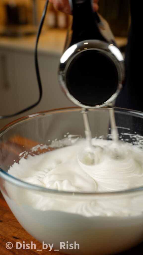 whisking egg whites in a large mixing bowl with electric whisk