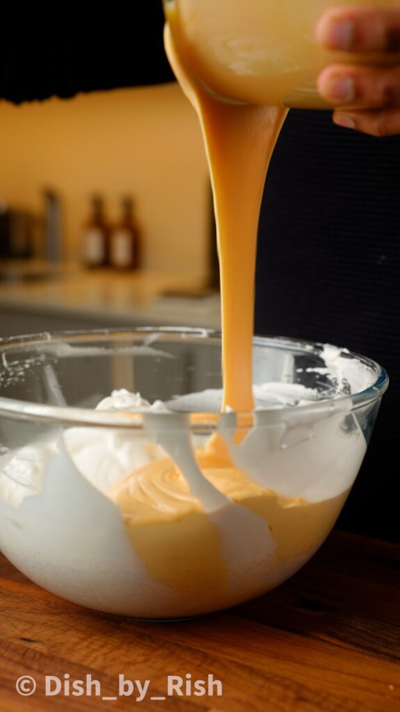 pouring lightened egg yolk mixture into egg white bowl