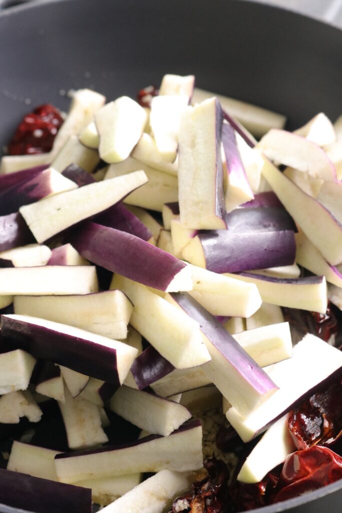 sliced aubergines added to wok