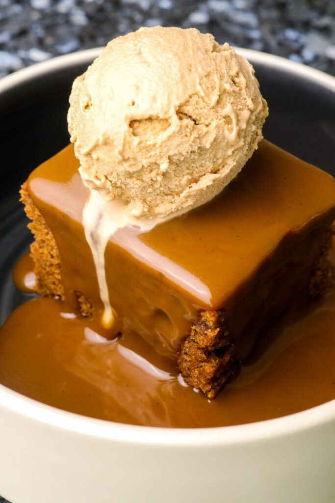 espresso caramel poured over slice of sticky toffee pudding with vanilla ice cream on top