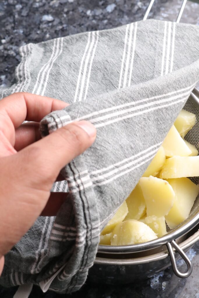 boiled potatoes cooling in a colander with a towel over them